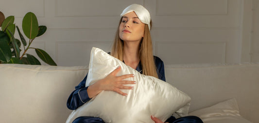 Woman wearing silk sleep eye mask holding a Silk Closet ivory silk pillow.