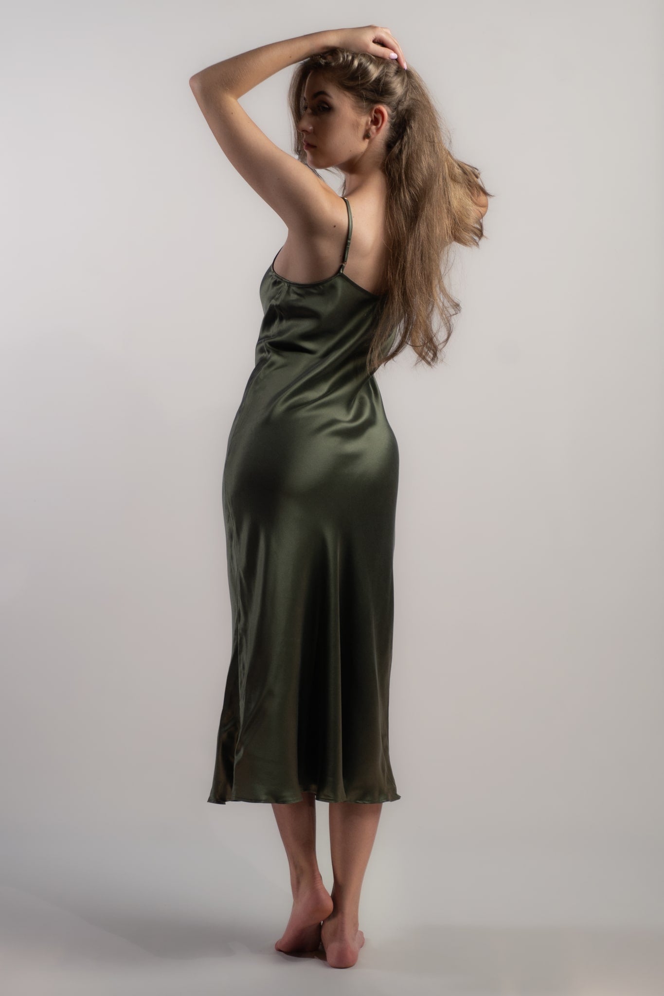 Woman wearing Silk Closet silk slip dress in olive green. 100% pure sandwashed silk with bias cut and adjustable spaghetti straps. 90s style dress.  Back view
