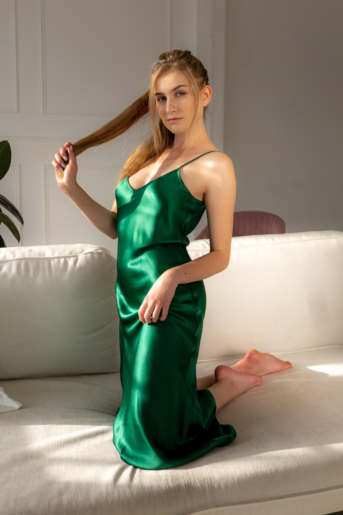 Woman wearing Silk Closet emerald green silk slip dress.  100% pure silk dress with bias cut and adjustable spaghetti straps. Kneeling on couch.