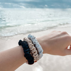 Black, silver and champagne silk midi hair scrunchies on arm at beach