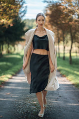 Model wearing Silk Closet black midi skirt and black crop blouse outdoors. Cream jacket