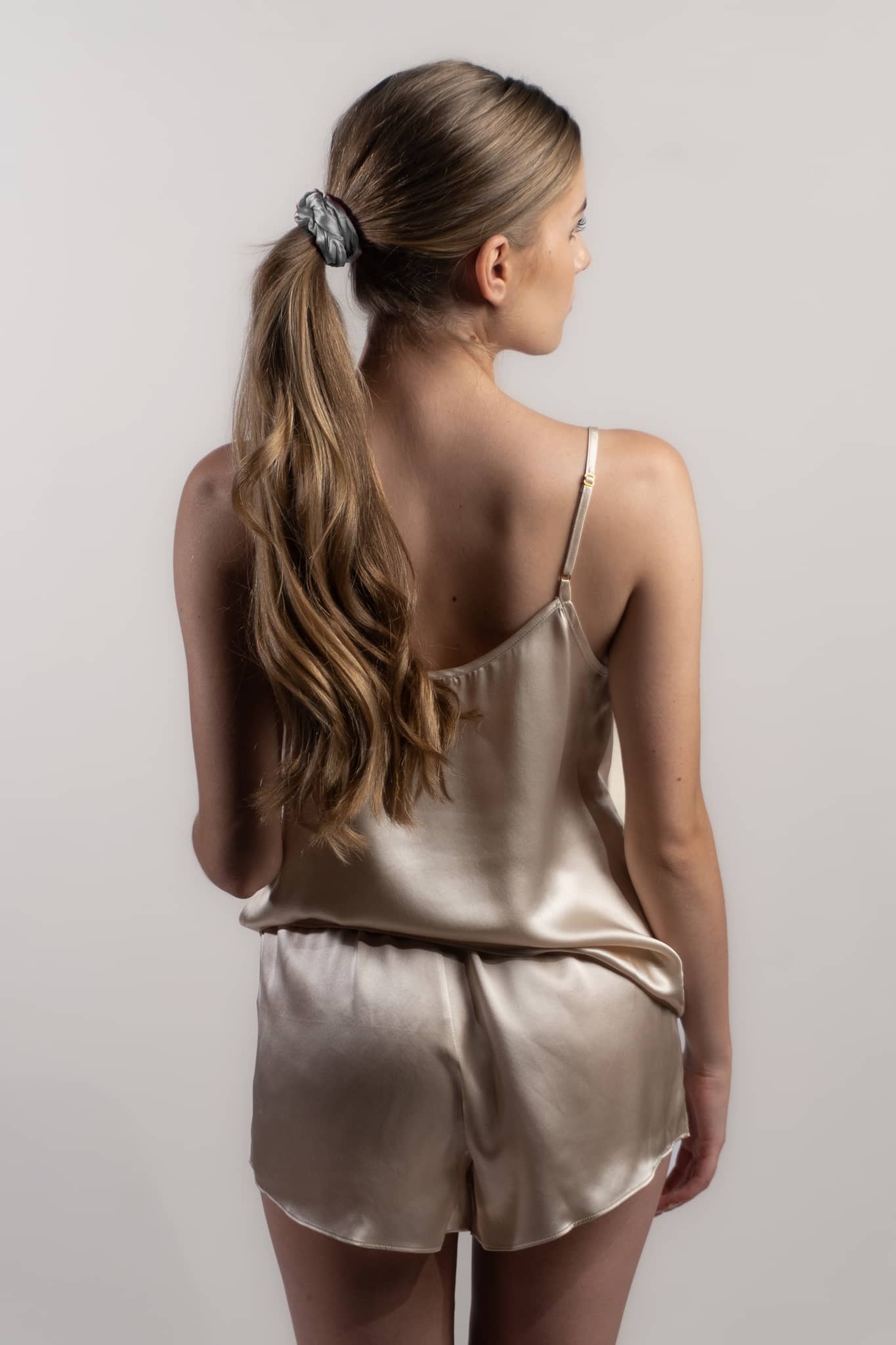 Woman wearing champagne coloured Silk Closet camisole and shorts set. Luxury sleepwear.  Back view.