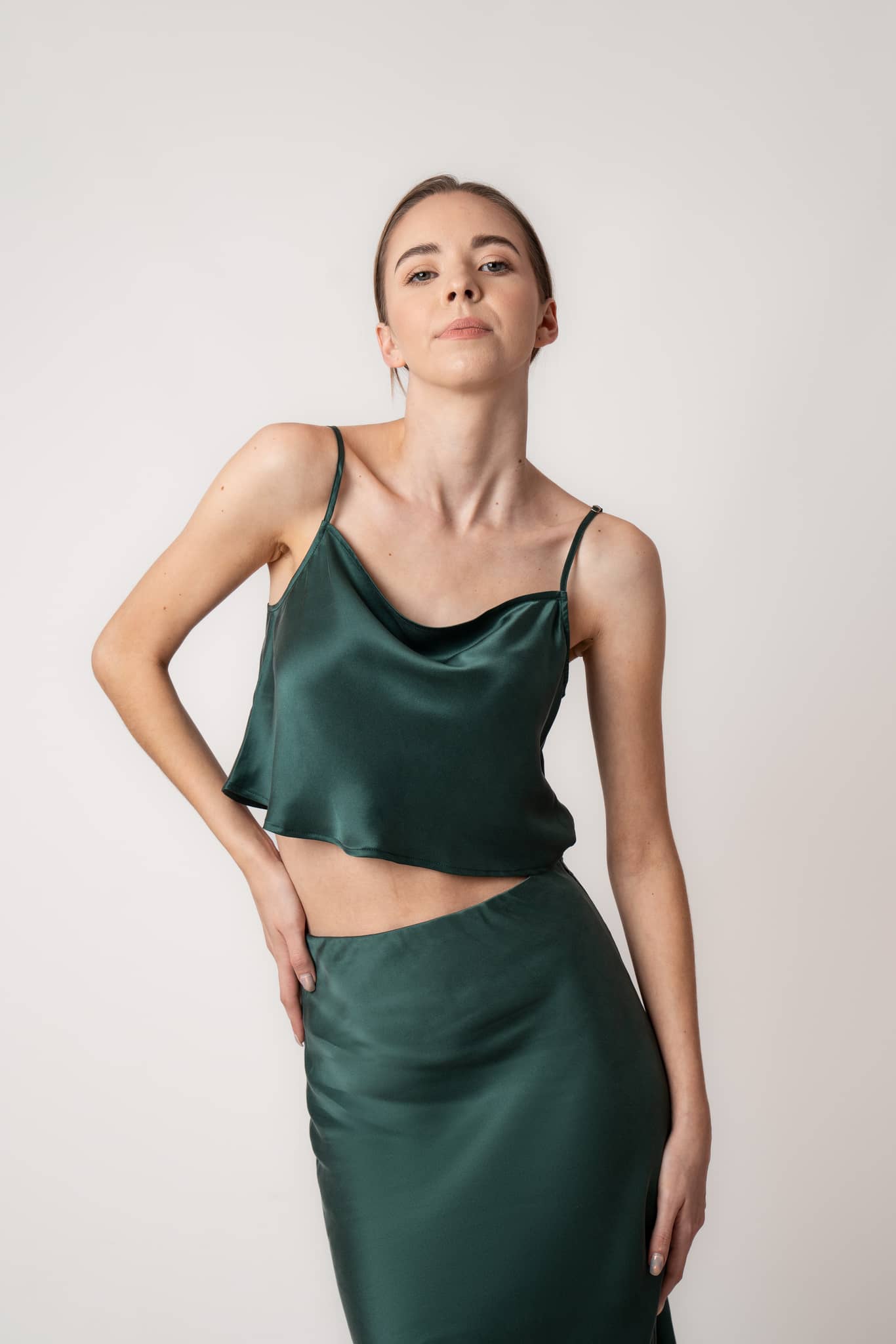 Woman sitting on couch wearing Silk Closet cowl neck sandwash silk green crop top and skirt in studio.