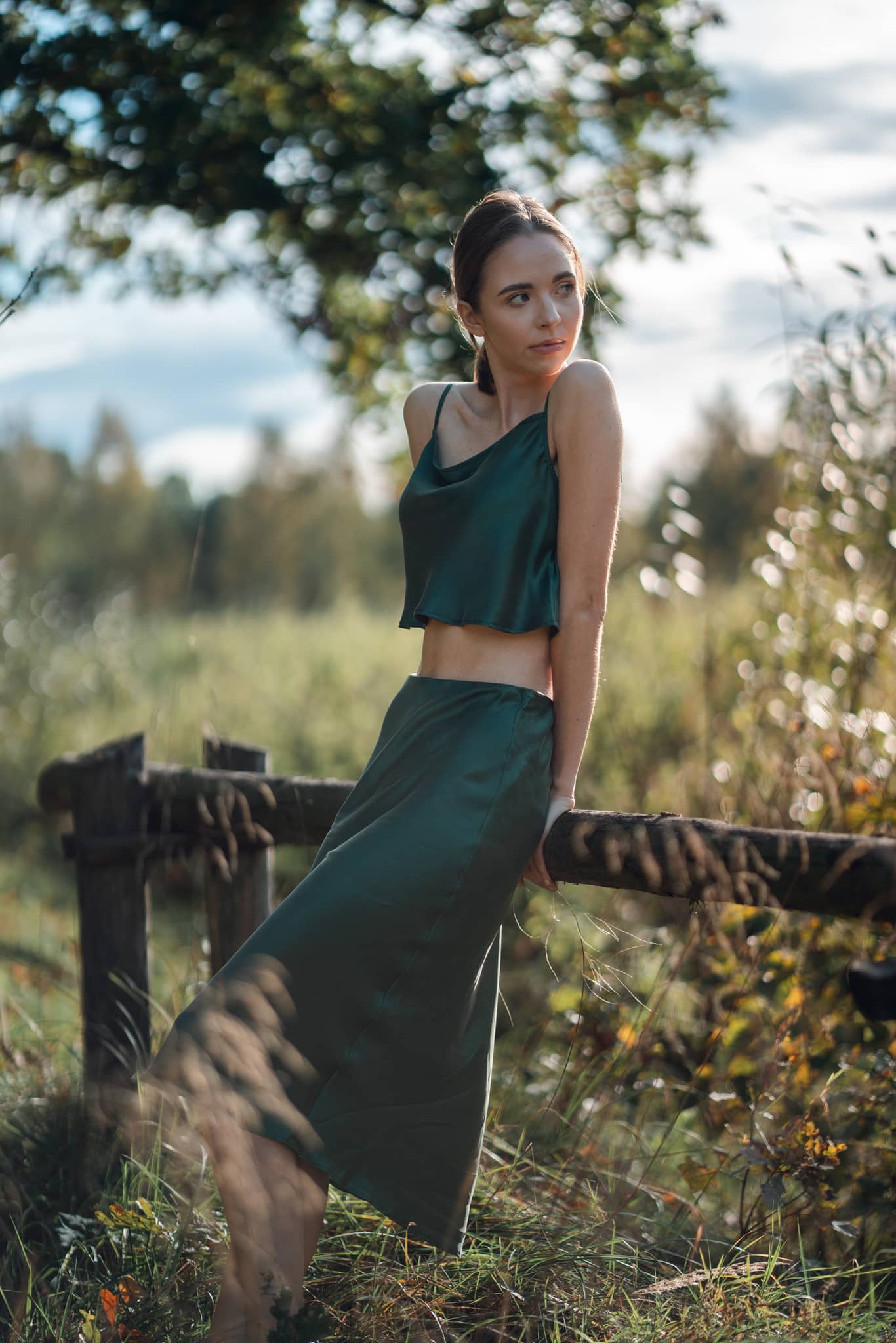 Woman sitting on couch wearing Silk Closet cowl neck sandwash silk green crop top and skirt