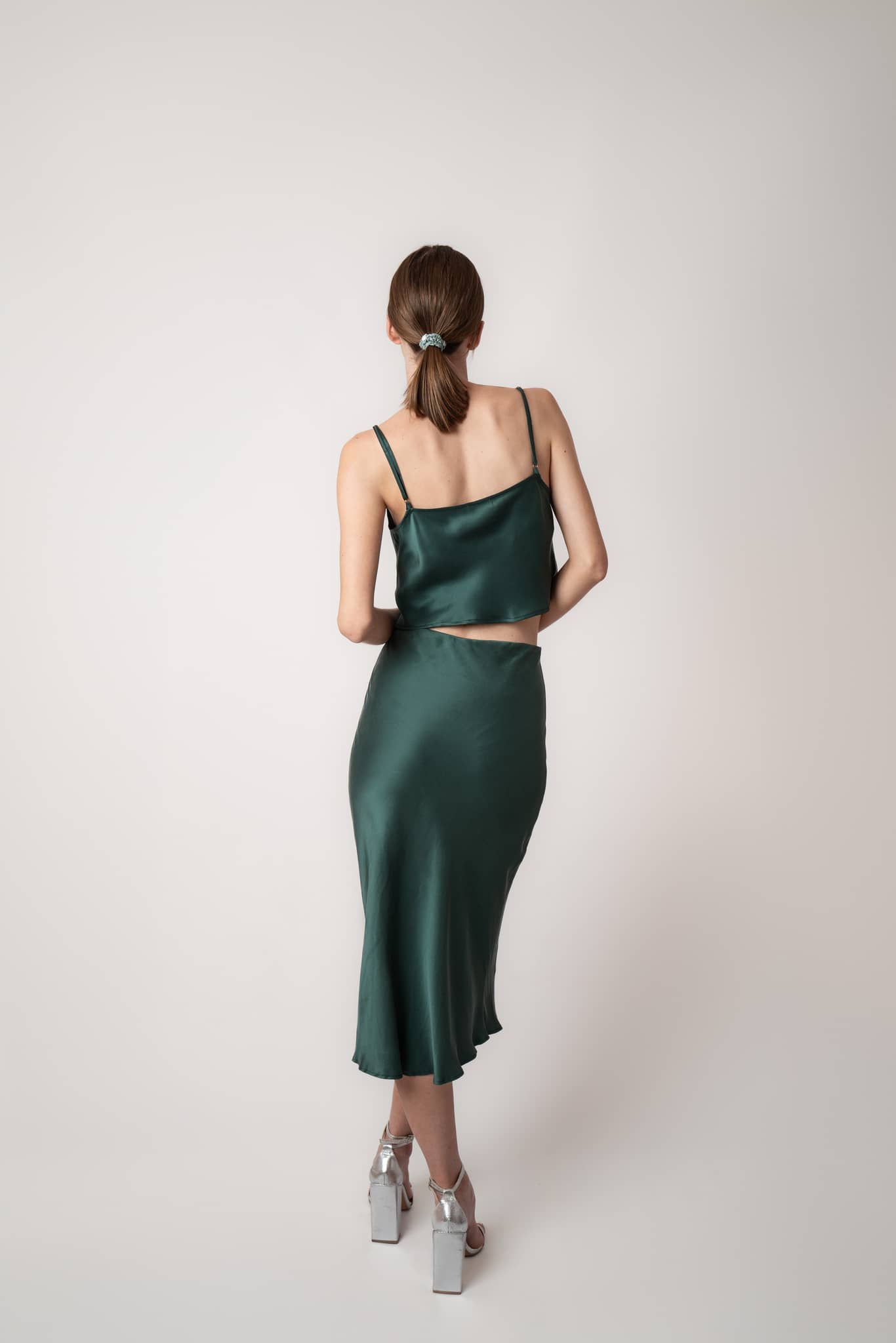 Woman sitting on couch wearing Silk Closet cowl neck sandwash silk green crop top and skirt back view