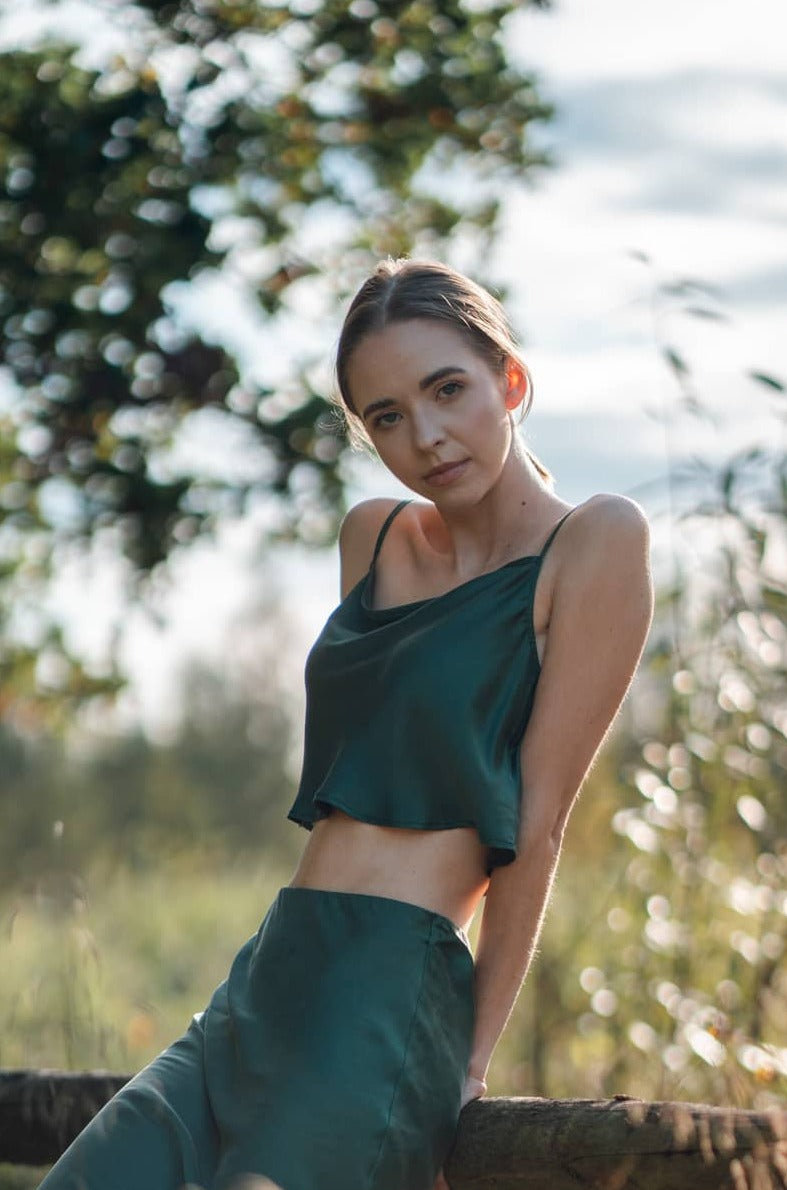 Woman sitting on couch wearing Silk Closet cowl neck sandwash silk green crop top and skirt in nature